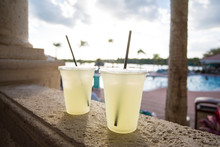 Two Delicious Glasses Of Lemonade Poolside At A Tropical Outdoor Resort. Selective Focus On The Two Glasses On A Hot Summer Day