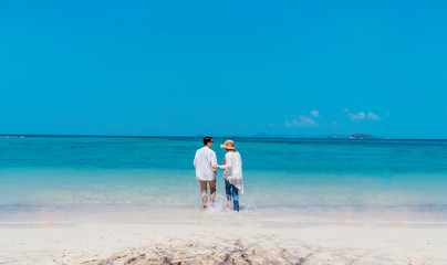 Wall Mural - Young happy couple white dress on seashore. Travel Vacation Retirement Lifestyle Concept. young couple holding hands and turn back on the beach in vacation day. summer time.