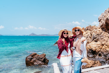 Wall Mural - confident young muslim friend of travellers on the beach. Travel concept. Tourist friend looking for take photo with sea background. two beautiful asian woman.