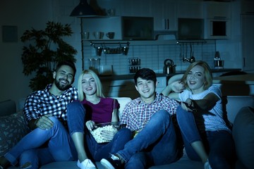 Wall Mural - Young friends with snacks watching TV on sofa at night