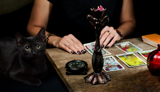 the fortune teller lays out on a wooden table the tarot cards by the light of a candle. black cat si