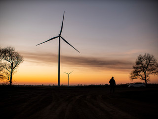 silhouette of a man goes to sunset in the direction of wind turbines