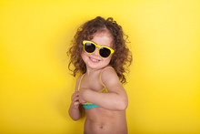 Little Girl In A Bathing Suit And Sunglasses On A Yellow Background