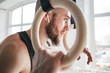Male bearded athlete with wireless headphones resting and holding gymnastics rings at light gym. Fit man relaxing on gymnastics rings after intense workout