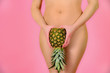 A young and sexy girl is holding a pineapple near the feet, on a pink background