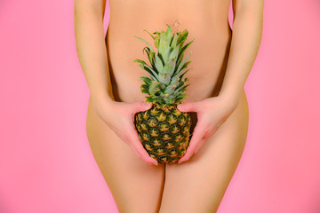 Wall Mural - A young and sexy girl is holding a pineapple near the feet, on a pink background