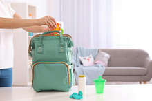 Woman Packing Baby Accessories Into Maternity Backpack On Table Indoors, Closeup