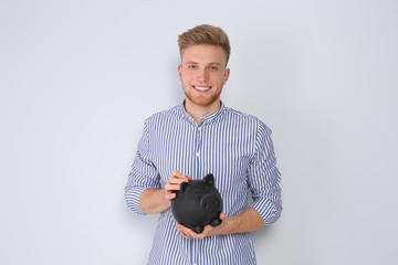 Wall Mural - Young man putting coin into piggy bank on light background