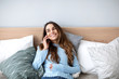 © BestForYou - Beautiful smiling woman talking on cellphone while lying in cozy bed at home.
