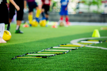 ladder drills on green artificial turf with blurry coach and kid soccer are training, blurry kid soccer jogging between marker cones and control ball with soccer equipment in soccer academy.