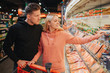 © estradaanton - Young couple in grocery store. They pick sea food together. Young woman point on mussels jar and smile. Man stand besides and hold hand on trolley.