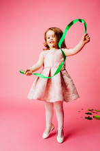 Portrait Of A Little Girl Playing With A Green Ribbon, Isolated On Pink
