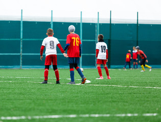 Boys in red white sportswear running on soccer field. Young footballers dribble and kick football ball in game. Training, active lifestyle, sport, children activity concept 