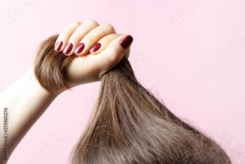Fotografía Female hands with red manicure holding hair, pink background, hair care concept