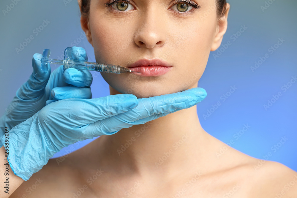 Young woman receiving injection in face on color background