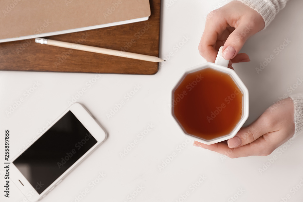 Female hands with cup of hot tea on white table