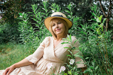 Beautiful blonde woman in hat and dress sitting on the grass