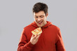 © Syda Productions - fast food and people concept - happy smiling young man in red hoodieeating pizza over grey background
