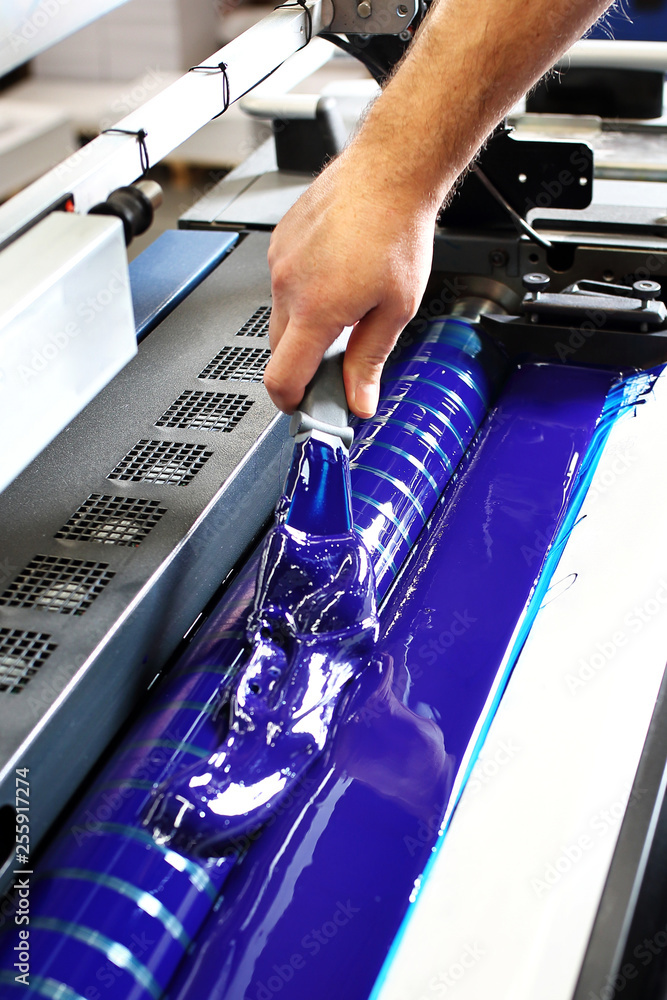 Drukarnia. Drukarz dolewa niebieską farbę drukarską do maszyny. - obrazy, fototapety, plakaty 