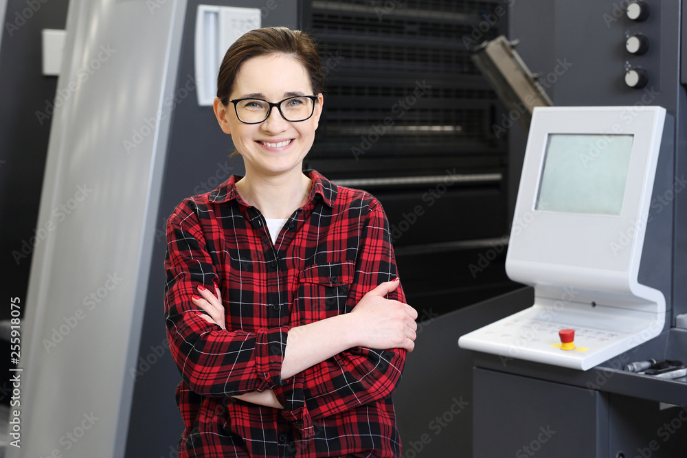 Drukarnia. Praca w drukarni. Uśmiechnięta kobieta, pracownik drukarni obsługuje maszynę drukarską. - obrazy, fototapety, plakaty 