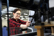 Drukarnia, introligatornia. Uśmiechnięta kobieta, pracownik drukarni stoi w hali produkcyjnej na tle nowoczesnych maszyn drukarskich