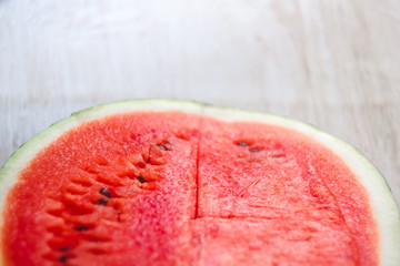 Wall Mural - Half a juicy watermelon on a light white wooden background, close-up. View from above