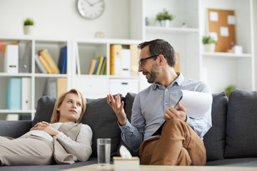 Wall Mural - Young patient lying on couch and looking at her psychologist near by explaining how to get out of despression