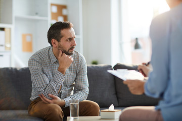 Wall Mural - Lonely and depressed man in casualwear thinking of his troubles while sitting on couch in front of psychologist