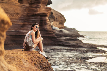 Wall Mural - Pretty long hair brunette tourist girl relaxing on the stones near sea.