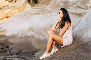 Wall Mural - Pretty long hair brunette tourist girl relaxing on the stones near sea.