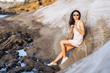 Wall Mural - Pretty long hair brunette tourist girl relaxing on the stones near sea.