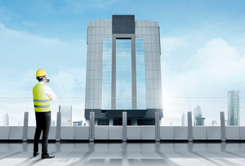  Rear view of asian worker man in safety vest, gloves, yellow helmet and protective mask standing on modern terrace and looking at skyscrapers