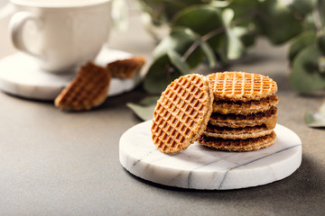 Mini stroopwafel, syrupwaffles cookies with cup of tea and eucalyptus twigs on light background with copy space.