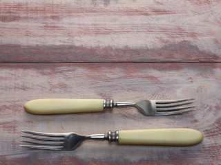 Two stainless steel forks with ivory handle on a brown wooden background with copyspace