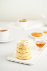 Wall Mural - Fried cheese cakes, sweet cheese pancakes on white plate on white background, vertical. Home tea party