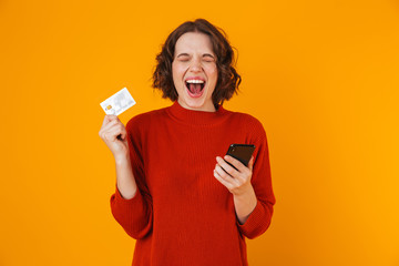 Poster - Portrait of attractive woman using cell phone and credit card while standing isolated over yellow background