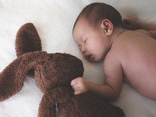 Asian female newborn baby sleeping in bed with dolls and sunlight in the morning. Cute little girl three weeks old.