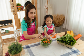 mother and daughter are helping to make vegetable salads in the kitchen on weekends h