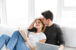 © Drobot Dean - Image of young couple using laptop and reading book while sitting on couch at home
