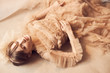 © monchak - Soft beauty portrait of young dreamy woman with blue eyes and bang, weared in nude tulle dress, with tulle hair accessory. The girl lies on the floor. Studio shot