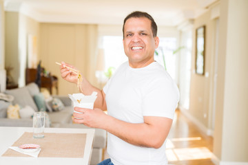 Middle age man eating take away noodles with choopsticks at home