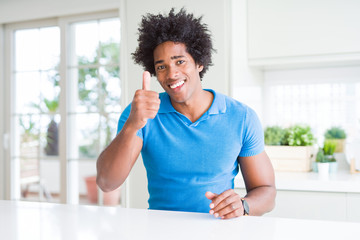 African American man at home doing happy thumbs up gesture with hand. Approving expression looking at the camera with showing success.