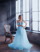A Gentle, Snow Queen Stands By The Window In A Fabulous Dress With Bare Shoulders. The Room Is Filled With Magical Rays Of Moonlight. An Image Of A Young Girl For The Prom Party. Art Photography