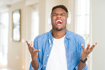 Poster - African american man wearing headphones listening to music celebrating mad and crazy for success with arms raised and closed eyes screaming excited. Winner concept