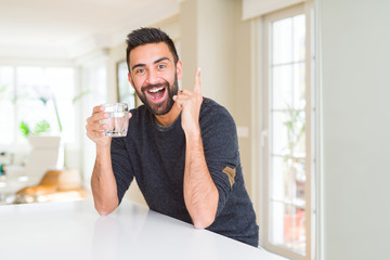 Handsome hispanic man drinking a fresh glass of water surprised with an idea or question pointing finger with happy face, number one