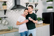 © sofiko14 - People, homosexuality, same-sex family, gay relationships concept. Male gay couple hugging each other and drinking their morning coffee while standing at the kitchen at home