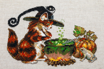 Cross-stitch embroidery with cat in hat, cauldron, toad, bonfire and pumpkin.