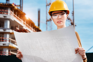 a beautiful young Asian woman civil engineer or architect is reviewing engineering plans in front of a construction site