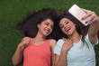 © IndiaPix - Top view of two smiling young girls lying on grass outdoors and taking selfie using mobile phone
