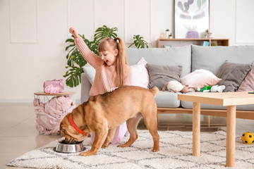 Cute little girl feeding funny dog at home